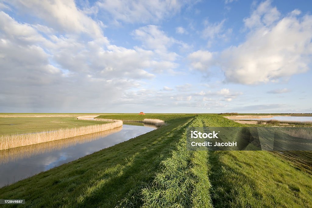 Dyke and Clouds Curved dyke along a canal with a cloudy sky above. Typical Dutch landscape in the Pettemerpolder between Petten and Camperduin, near the Hondsbossche Zeewering. Agriculture Stock Photo