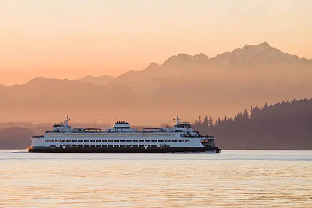 A Washington State Ferry traveling across Puget Sound at sunset with the Olympic Mountains in the background.