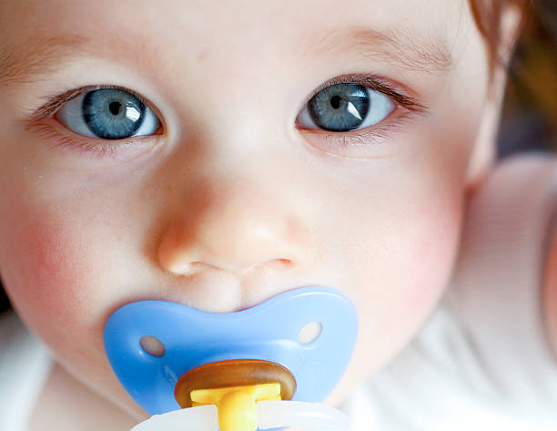 Close-up of blue-eyed baby with blue pacifier stock photo