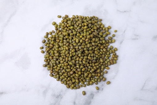Pile of green mung beans on white marble table, top view