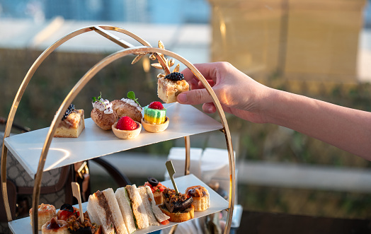 Woman's hand gently take a dessert from a tall sweet treat display set in an elegant afternoon tea restaurant