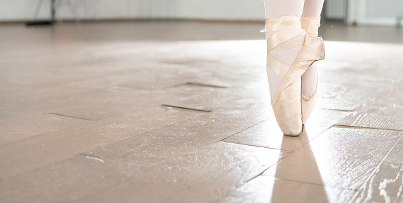 close up on ballerina feet; ballet dancer practicing in a dance studio with wooden floor, ballerina pointe shoes in action