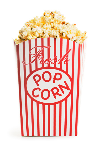A movie theater popcorn box heaped with the fresh popped, crispy, salty, buttered snack. Served in classic red and white striped paper containers, the delicious film entertainment event treat can be shared with a date for nightlife food of unhealthy eating. Front view, cut out and isolated on white background.