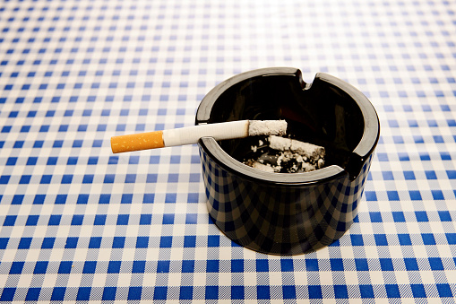 Full ashtray with cigarette butt, which stands on a wooden table