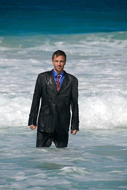 Businessman Got a Soaking "Businessman stands in the middle of rushing waves, soaking wet" soaked suit stock pictures, royalty-free photos & images