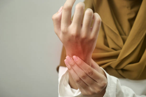 Anonymous woman touching her wrist, suffering from arthritis disease, close up against grey stock photo