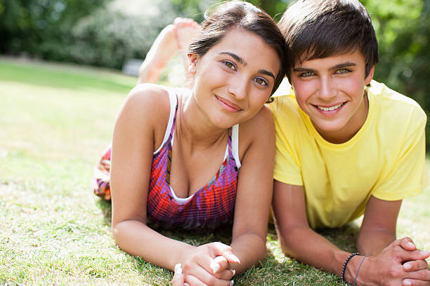 lächelnd teenager paar auf gras zusammen verbringen - teenage couple stock-fotos und bilder