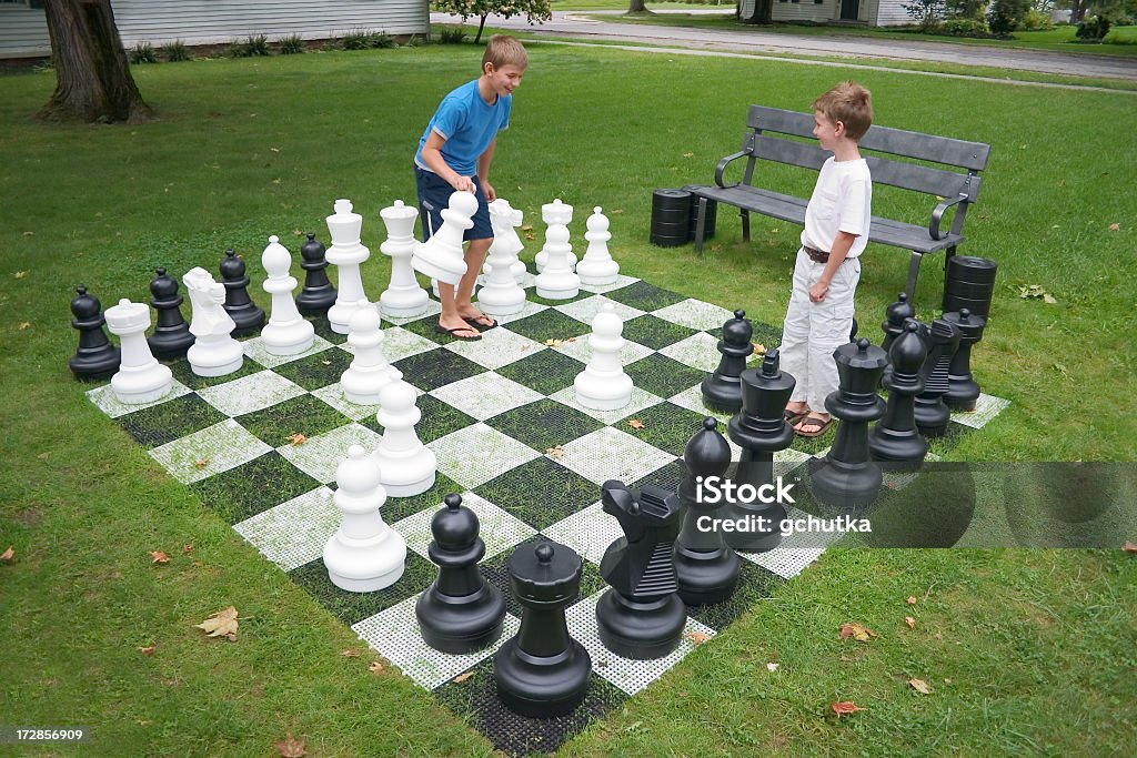 Two kids playing a chess game with large pieces on grass Young boys playing lawn chess. Chess Stock Photo