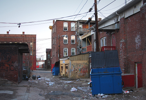 Trash filled urban alleyway in a run down inner city urban neighborhood in Holyoke, Massachusetts surrounded by large brick tenements. American inner cities remain concentrations of poverty, homelessness, unemployment, crime, and drugs.
