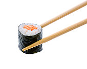 A sushi roll with salmon being held by wooden chopsticks