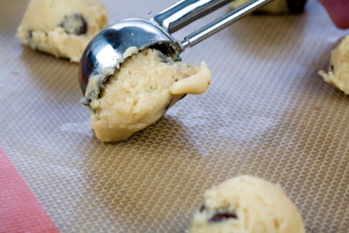 Closeup of a chocolate chip cookie being placed on a baking sheet.
