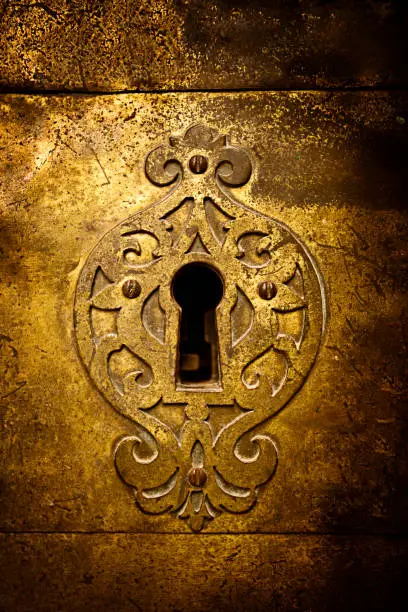 An old medieval keyhole on a gold / brass door with a rutsy ornate plate.