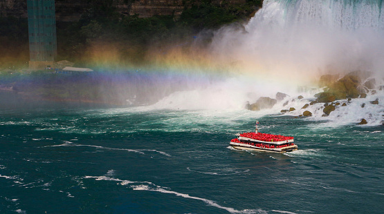 Close up of The Hornblower cruise boat traveling under a rainbow in front of the American Falls of Niagara Falls.