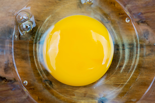 Close up fresh egg yolk on glass of bowl over wooden background