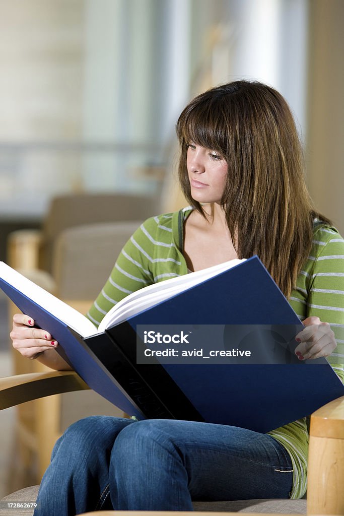 Молодая женщина, чтение большая Книга в библиотеке - Стоковые фото Книга роялти-фри