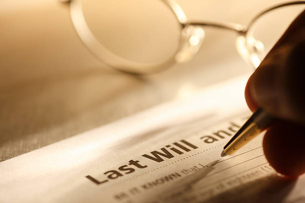 Man signing last will and testament A close up of a man signing his last will and testament.  A pair of eyeglasses rest on the desktop in the background.  A warm color scheme dominates the scene. A strong directional light casts a strong shadow across the image. last stock pictures, royalty-free photos & images