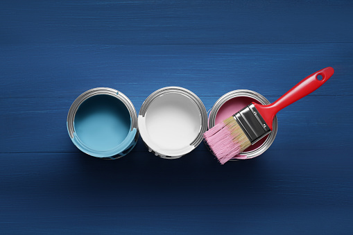 Cans of paints and brush on blue wooden background, flat lay