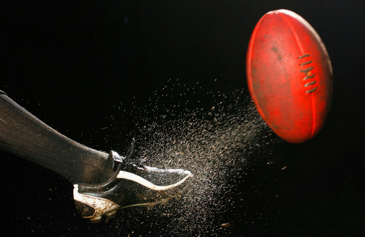 Water and mud fly as an AFL ball is kicked in front of a black background