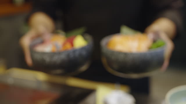 Chef placing salmon and assorted fish sashimi bowls on service counter ready to be served and continue cooking behind the kitchen counter at a sashimi restaurant.