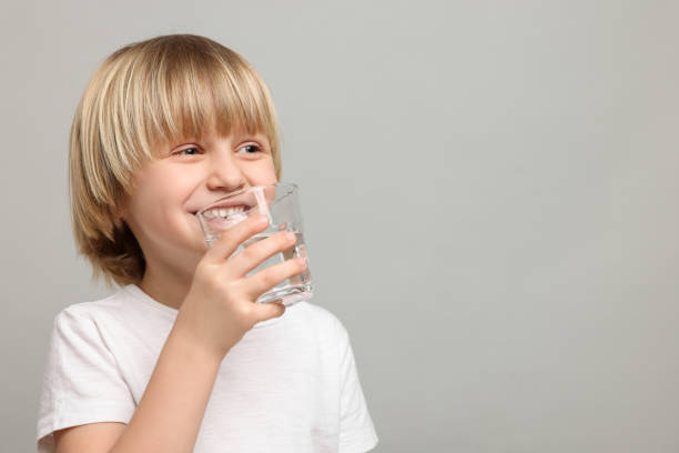 istock Happy little boy drinking fresh water on light grey background. Space for text 1728644880