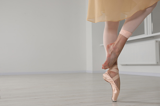 Ballerina in pointe shoe dancing indoors, closeup. Space for text