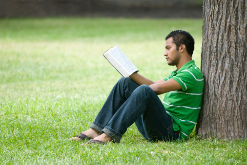 Man reading a paperback book in a public park.