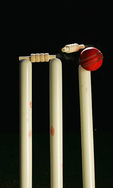 Red cricket ball hitting right wicket out with bail falling A cricket ball crashes through a set of stumps cricket stump photos stock pictures, royalty-free photos & images
