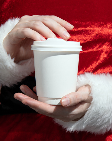 Composite image of a girl in a Santa costume holding a white paper cup. close-up