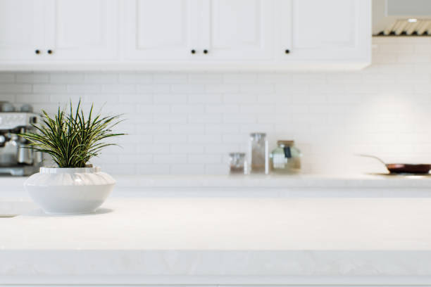 istock Modern white kitchen countertop with indoor plants and advertising space mounting your product on a blurred kitchen space in the background. 3D rendering. 1728682506