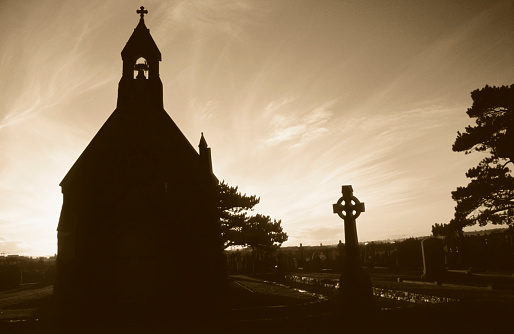 The silhouette of a little chapel and a celtic cross on the cemetery of Galway, Ireland, the sunset in the background makes it a beautiful back light composition.