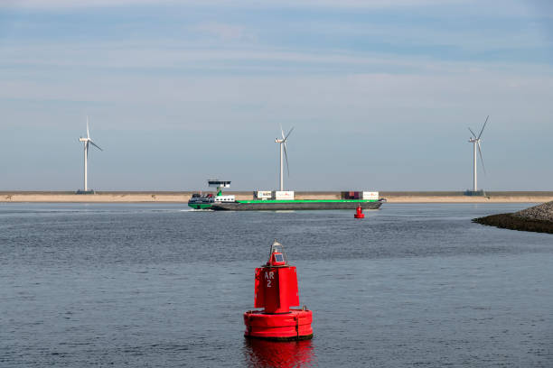 Rotterdam, the Netherlands-September 16, 2023; Inland container vessel in the Prinses Arianehaven (harbor) on the Maasvlakte with red buoy in front and modern wind turbines in background