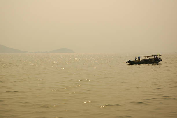 Fishing Boat at Dusk on Lake Tai "Fishing boat at dusk on Lake Tai, Wuxi, China.  Heavy haze and the sun produces a natural sepia toned effect." lake tai stock pictures, royalty-free photos & images