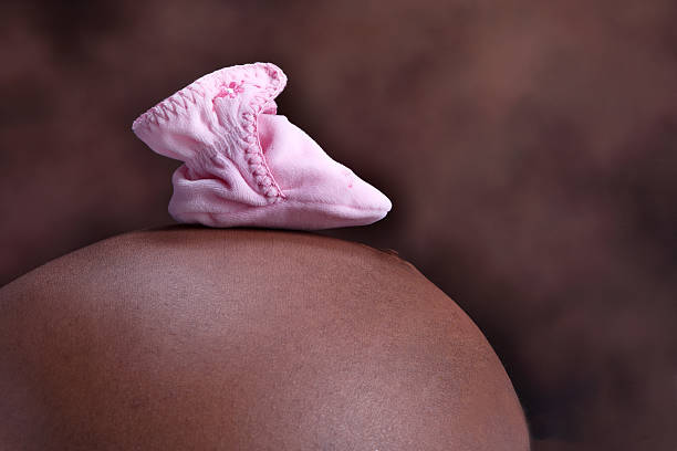 A pink baby bootie rests on a pregnant woman's belly. Shot with Canon 1D Mark III.