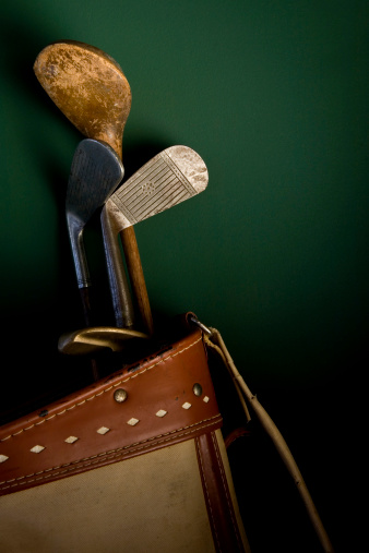 A few antique golf clubs in an old golf bag leaning against a painted wall.