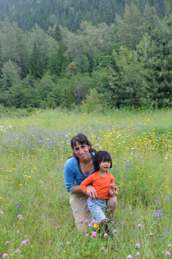 A mother and her daughter smile and hold hands in a flower-filled meadow.