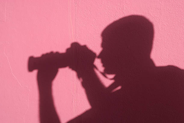 Shadow man on pink wall uses a zoom lens to take a photo far away