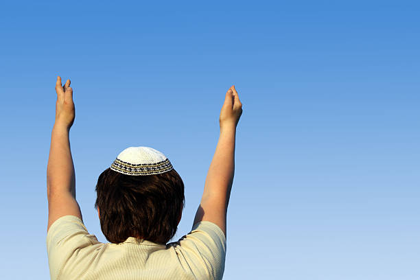 Boy, seen from behind, praying and reaching to the sky stock photo