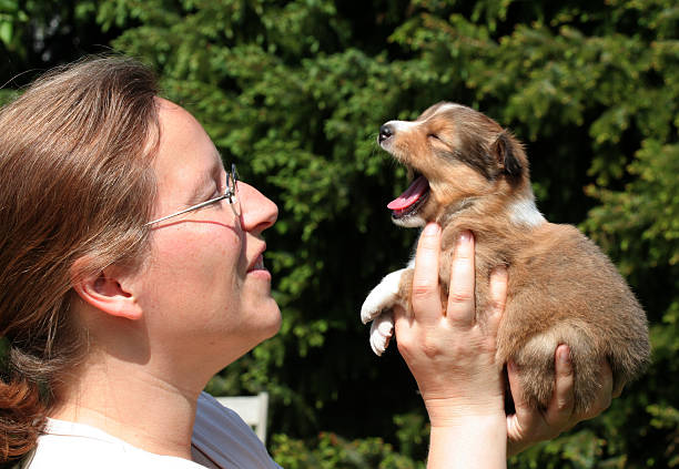 Woman holding a three weeks old puppie in one hand.