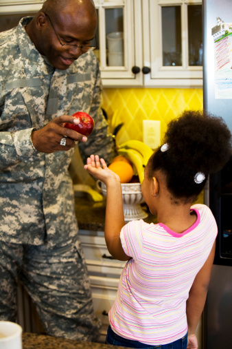 African American father giving his daughter an apple in the kitchen.  Focus is on the apple.