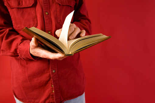 Man reading book. He wears a red shirt and stands against a red background.