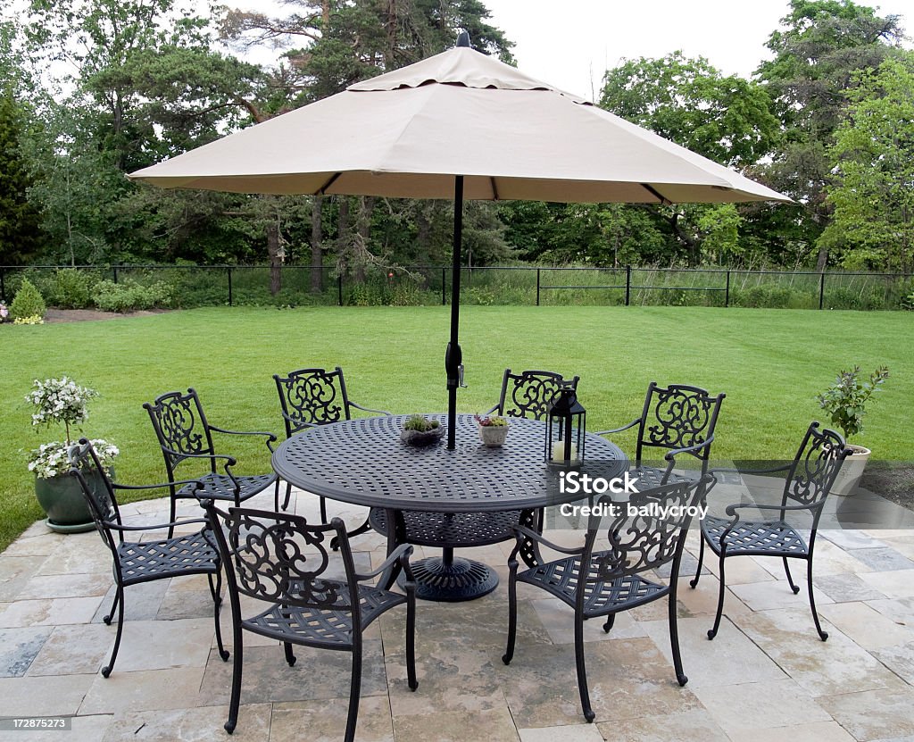 Black metal patio furniture set with tan umbrella Rod iron patio furniture on a beautiful flagstone patio. Patio Umbrella Stock Photo