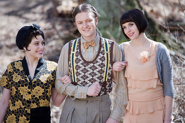One lucky man walks in the park with two women all in 1920s style clothing.