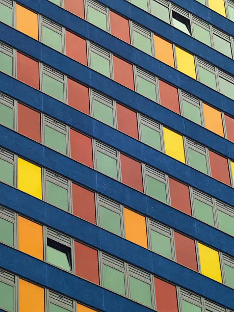 "A city-centre office building with multi-coloured panels. Two windows are open - one at bottom left, one at top right."