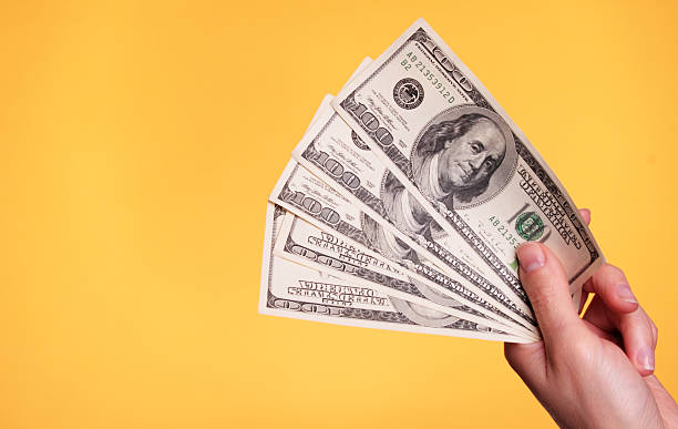 A hand holding five $100 bills Woman holding 500 dollars against a yellow background. currency photos stock pictures, royalty-free photos & images