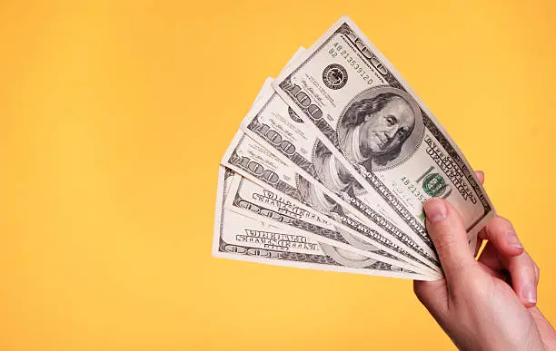 Woman holding 500 dollars against a yellow background.
