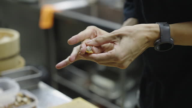Close-up of chef's hands molding vinegared rice into small ball and placing grilled freshwater eel or unagi eel on top to make unagi nigiri sushi and putting it on serving plate on kitchen counter.