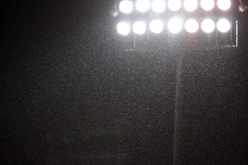 Bright stadium lights shining through the pouring rain during a rained out MLB game.