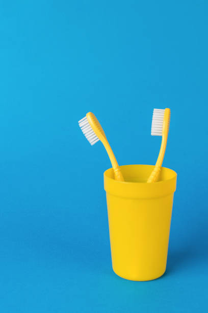 istock Two yellow toothbrushes in a yellow plastic cup on a blue background. 1728791557