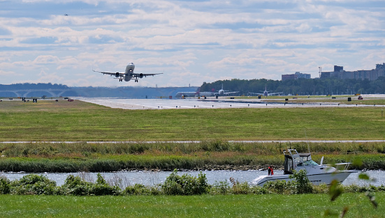 A commercial airliner takes off from Reagan National Airport in Arlington, Virginia in the background while a Striper fishing boat with one passenger passes by in the foreground.