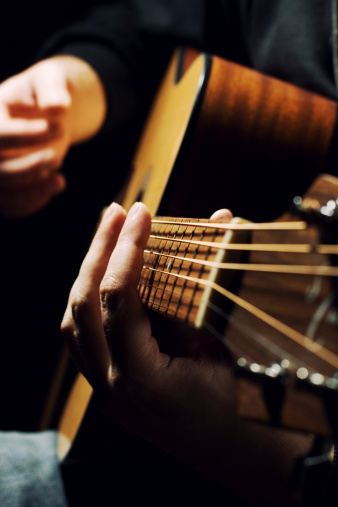 Close-up on the hands of a man playing classical guitar, seated on a leather armchair. The hand strumming the strings is out of focus.